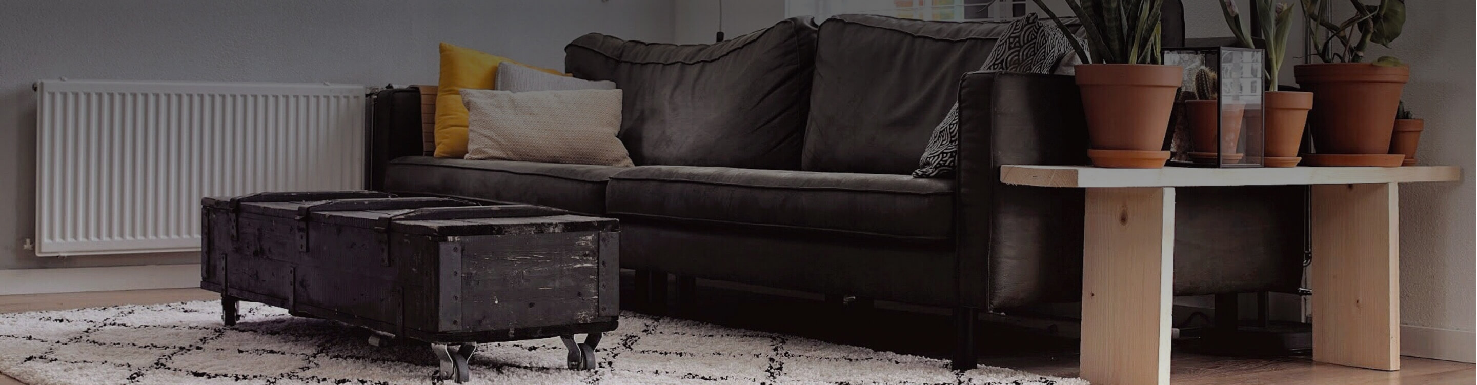 Brown couch on a pattered white and grey area rug with a industrial design coffee table.